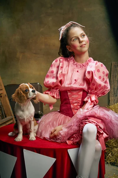 Circus show with animal handler. Little cute beautiful girl in festive dress training funny doggy at vintage circus. Concept of holidays, dreams, art, fashion, vintage style