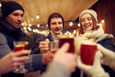 Noel havası. Sıcak giysiler içinde neşeli erkek ve kadınlar kış festivalinde sıcak içeceklerle birlikte vakit geçiriyorlar. Eğleniyorlar, sıcak giyiniyorlar, birbirlerine bakıyorlar ve gülüyorlar.