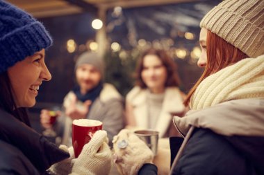 Dostça bir parti. Emotif gülümseyen erkekler ve kadınlar ellerinde kupalar dolusu sıcak şarapla eğleniyorlar, kış fuarında birlikte vakit geçiriyorlar. Keyif alıyorlar, sıcak giyiniyorlar.