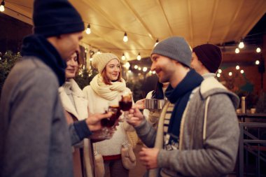 Eğlence, neşe, parti. Bir grup genç birlikte vakit geçiriyor, sıcak şarap içiyor, konuşuyor, kış festivalinde gülüyor. Gençlik sıcacık giyiniyor. Kış tatili, Noel heyecanı konsepti.