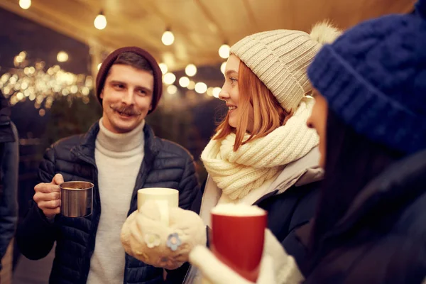 一群年轻人一起消磨时光 喝着含酒精的葡萄酒 晚上在冬日的集市上大笑 年轻人穿得很暖和 圣诞气氛概念 — 图库照片