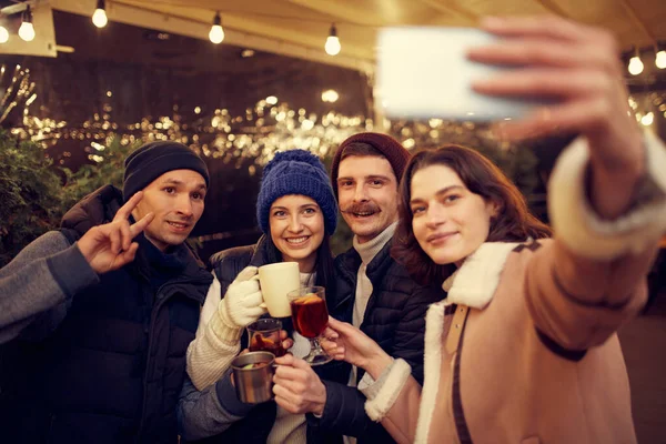 Selfie çekiyorum. Emotif gülümseyen erkekler ve kadınlar ellerinde kupalar dolusu sıcak şarapla eğleniyorlar, kış fuarında birlikte vakit geçiriyorlar. Keyif alıyorlar, sıcak giyiniyorlar.