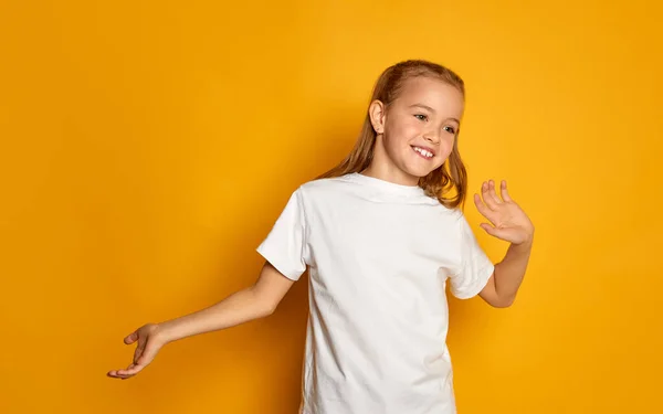 一个漂亮的小女孩的画像 穿着白色T恤的孩子摆着姿势 在黄色的工作室背景上愉快地与人隔离交谈 面部表情 生活方式的概念 — 图库照片