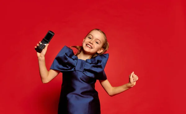 一个漂亮的小女孩的画像 穿着衣服的孩子在红色的工作室背景下摆出一副手机的姿势 面部表情 生活方式的概念 — 图库照片