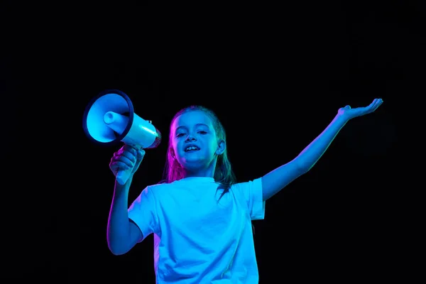 一个漂亮的小女孩的画像 穿着白色T恤的孩子摆着姿势 在霓虹灯下 在黑色背景上与扩音器对话 面部表情 生活方式的概念 — 图库照片
