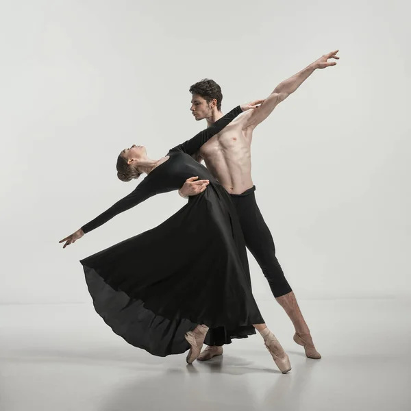 Young muscular man and woman in black silk dress, ballet dancers performing isolated over grey studio background. Concept of classical dance aesthetics, choreography, art, beauty. Copy space for ad