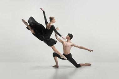Genç adam ve kadın, bale dansçıları gri stüdyo arka planında izole bir şekilde gösteri yapıyorlar. Halat atlayışı. Klasik dans estetiği, koreografi, sanat, güzellik kavramı. İlan için alanı kopyala