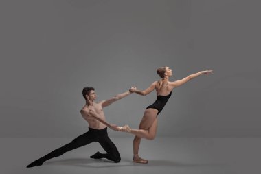Genç adam ve kadın, bale dansçıları koyu gri stüdyo arka planında soyutlanmış bir şekilde gösteri yapıyorlar. Bilmece pozisyonu. Klasik dans estetiği, koreografi, sanat, güzellik kavramı. İlan için alanı kopyala