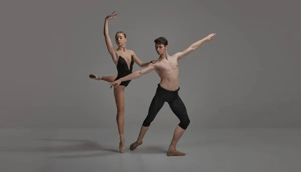 Young man and woman, ballet dancers performing isolated over dark grey studio background. Artistic movements. Concept of classical dance aesthetics, choreography, art, beauty. Copy space for ad