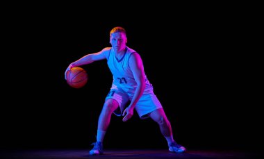 Genç aktif sporcunun dinamik portresi, spor üniformalı erkek basketbolcu topla antrenman yapıyor, zıplıyor, neon ışıkta karanlık arka planda salya akıtıyor. İlan için alanı kopyala