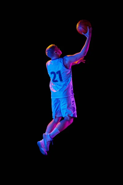 大きなエネルギーだ 若いアクティブな選手のスタジオショット ネオンの光の暗い背景の上に隔離されたボールと動きとアクションのスポーツのユニフォームの男性バスケットボール選手 広告のコピースペース — ストック写真
