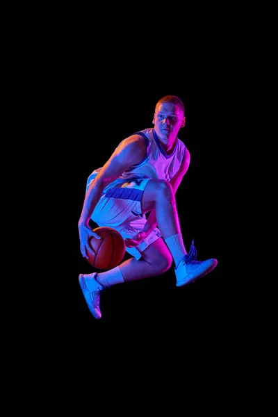 行动中 在紫色霓虹灯下 活跃的男性篮球运动员在黑暗背景下与篮球一起跳跃 职业体育 业余爱好 竞赛的概念 — 图库照片