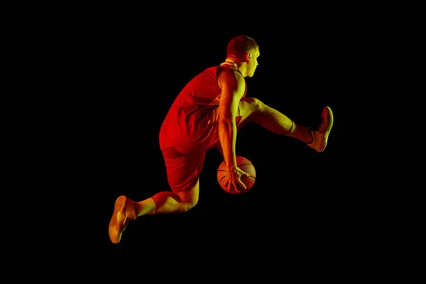 巨大的能量 演播室拍摄年轻活跃的运动员 身穿运动服的男性篮球运动员在运动 在霓虹灯下在黑暗背景下与球隔离的动作 广告的复制空间 — 图库照片