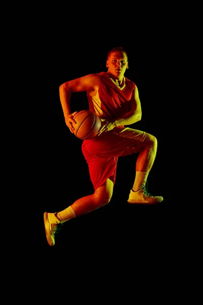 大きなエネルギーだ 若いアクティブな選手のスタジオショット ネオンの光の暗い背景の上に隔離されたボールと動きとアクションのスポーツのユニフォームの男性バスケットボール選手 広告のコピースペース — ストック写真