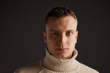 Koyu gri stüdyo arka planında, şık süveter giyen yakışıklı bir adamın portresi. Dikkatli bak. Erkek sağlığı, yaşam tarzı, moda, duygular, refah kavramı. İlan için alanı kopyala