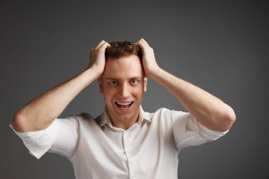 Duygusal olarak beyaz gömlekle poz veren genç bir adamın portresi gri stüdyo arka planında izole edilir. Şok oldum, şaşırdım. Erkek sağlığı, yaşam tarzı, moda, duygular, refah kavramı. İlan için alanı kopyala