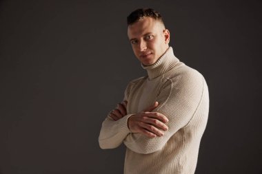 Koyu gri stüdyo arka planında, şık süveter giyen yakışıklı bir adamın portresi. Acımasız iş adamı. Erkek sağlığı, yaşam tarzı, moda, duygular, refah kavramı. İlan için alanı kopyala