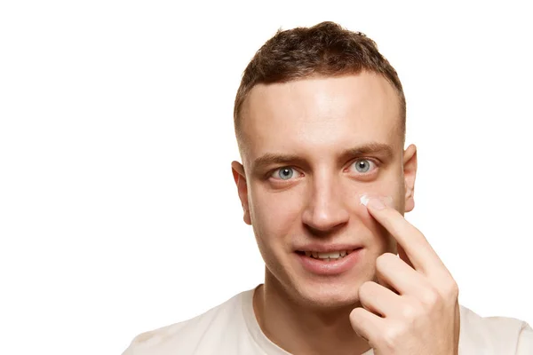 白いスタジオの背景に孤立した顔のクリームを適用する若い男のクローズアップ肖像画 男性化粧品 男性の健康 セルフケア ボディケア スキンケアの概念 広告のコピースペース — ストック写真