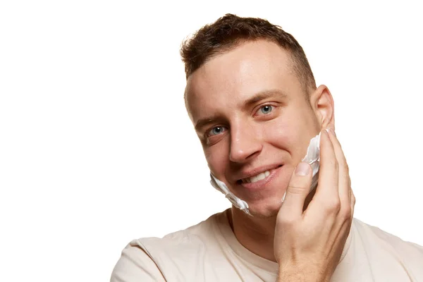 白いスタジオの背景に隔離されたポーズをとって フェイスシェービングクリームを適用した若い陽気な男の肖像画 男性の健康 セルフケア ボディケア スキンケアの概念 広告のコピースペース — ストック写真