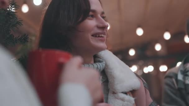 专注于穿着冬衣的年轻貌美的女孩 喝着热饮 做着白日梦 晚上和朋友一起在冬天的集市上消磨时间 看起来很高兴 很高兴 — 图库视频影像