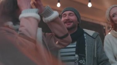 Bir grup mutlu erkek ve kadın dans ediyor, eğleniyor, kış festivalinde akşam vakti dışarıda vakit geçiriyorlar. Eğleniyorlar, sıcak giyiniyorlar, birbirlerine bakıyorlar ve gülüyorlar.