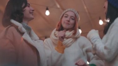 Bir grup mutlu erkek ve kadın dans ediyor, eğleniyor, kış festivalinde akşam vakti dışarıda vakit geçiriyorlar. Eğleniyorlar, sıcak giyiniyorlar, birbirlerine bakıyorlar ve gülüyorlar.