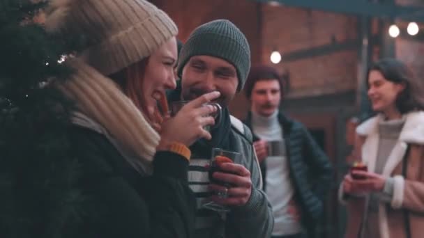 クリスマス気分 暖かい服を着た若い陽気な男性と女性が熱い飲み物で冬の伝統的なフェアで一緒に時間を過ごす 楽しく 暖かく お互いを見て 笑って — ストック動画
