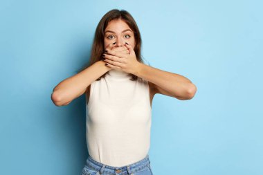 Güzel bir kadının portresi. Mavi arka planda elleri kapalı, ağzı kapalı poz veriyor. Sessizlik! Sırlar. Gençlik kültürü kavramı, duygular, yüz ifadesi, moda. İlan için alanı kopyala