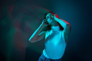 Genç ve güzel bir kadının portresi, duygusal danslar, neon ışıklarıyla izole edilmiş mavi stüdyo arkaplanı. Gençlik kültürü kavramı, duygular, yüz ifadesi, moda. İlan için alanı kopyala