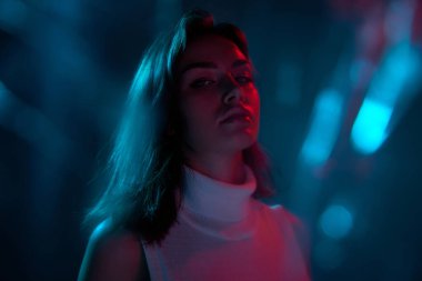 Genç ve güzel bir kadının portresi, mavi arka planda izole edilmiş kameraya bakıyor neon ışıkta. Bokeh etkisi. Gençlik kültürü kavramı, duygular, yüz ifadesi, moda. İlan için alanı kopyala