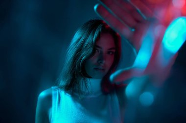 Mavi stüdyo arka planında neon ışıklarıyla izole edilmiş güzel bir kadının portresi. Bokeh etkisi. Gençlik kültürü kavramı, duygular, yüz ifadesi, moda. İlan için alanı kopyala