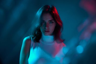 Genç ve güzel bir kadının portresi dikkatlice kameraya bakıyor mavi arka planda neon ışıkta izole edilmiş. Gençlik kültürü kavramı, duygular, yüz ifadesi, moda. İlan için alanı kopyala