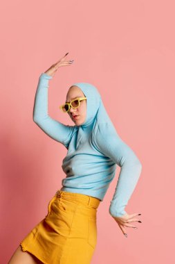 Tuhaf insanlar konsepti. Pembe arka planda yalnız poz veren yenilikçi moda kıyafetli genç kızın yaratıcı portresi. Canlı stil, nonoş, sanat, moda modeli mavi süveter içinde.