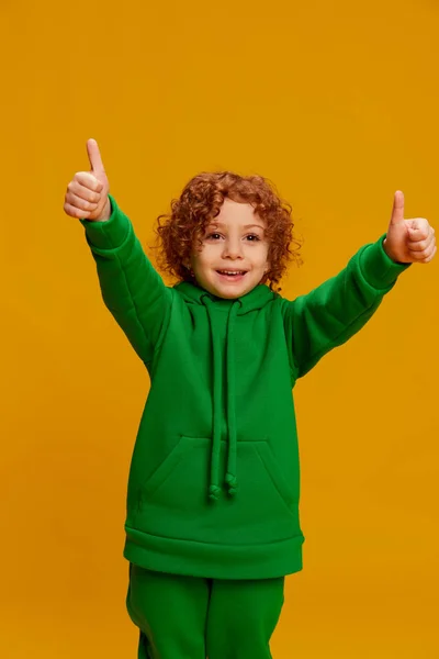 stock image Portrait of little girl, child with curly red hair posing, showing cheerful emotions isolated over yellow background. Concept of childhood, positivity, lifestyle, fashion, happiness. Copy space for ad