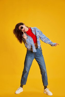 Şık giyinmiş güzel bir kızın portresi, sarı arka planda izole edilmiş bir şekilde şarkı söylüyor. Gençlik kavramı, güzellik, moda, yaşam tarzı, duygular, yüz ifadesi. Ad