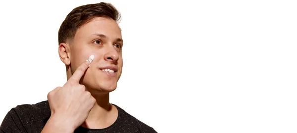 面部皮肤对男人的护理 年轻迷人的男子完美地保存皮肤使用面霜隔离在白色背景 化妆品 美容美发广告的复制空间 — 图库照片