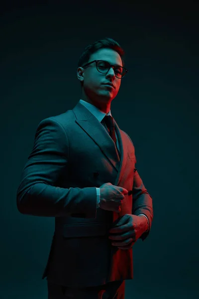 Confidence. Fashionable young businessman in classic style suit adjusting jacket isolated over dark background in neon light. Concept of business, fashion, style, modern lisfestyle.