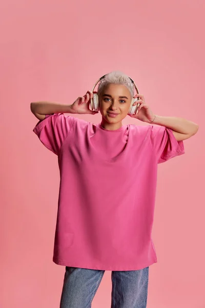 穿着休闲装 穿着短发 头戴耳机 背景粉色的年轻时尚女性的肖像 生活方式 面部表情的概念 — 图库照片