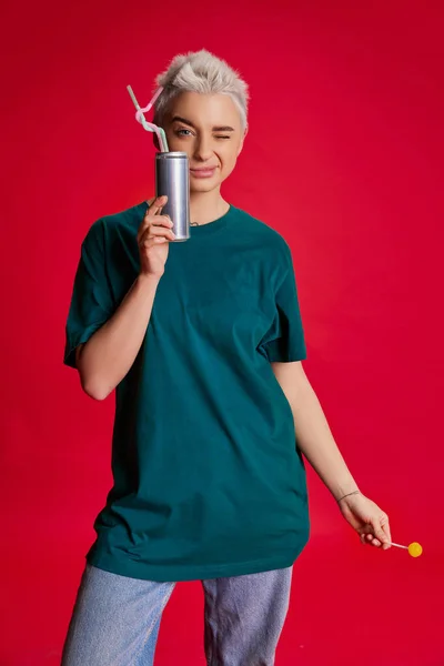 年轻而时尚的女人 留着短发 穿着舒适的休闲服 喝着红背景的可乐 生活方式 面部表情的概念 — 图库照片