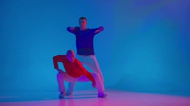 Neon ışıklarıyla dans salonundaki mavi arka planda deneysel dans eden sportif kıyafetli iki dansçı. Modern gençlik kültürü, hareketler, tarz ve moda kavramı, eylem.