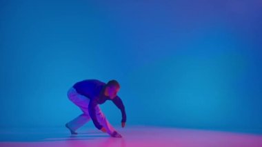 İfade. Genç enerjik adam dans ediyor parlak spor kıyafetlerle neon dans salonunda mavi arka planda deneysel dans yapıyor. Modern gençlik kültürü, stil ve moda kavramı, eylem.