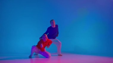 Müziği. Şık erkek ve kadın parlak spor kıyafetlerle neon ışıkta dans pistinde dans ediyorlar. Modern gençlik kültürü, hareketler, tarz ve moda kavramı, eylem.