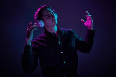 Gündelik siyah gömlekli genç adam portresi Heapholnes 'de müzik dinlerken neon ışıkta koyu mor arka planda izole edilmiş. İnsan duyguları kavramı, yüz ifadesi, satış, reklam, moda