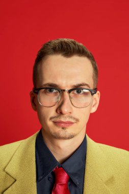 Kırmızı arka planda poz veren şık ceketli ve gözlüklü genç bir adam portresi. Ciddi bir özenli yüz. Takım lideri. Duygular, iş, meslek, hobi, yaşam tarzı, moda kavramı