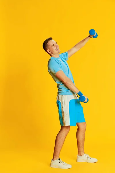 Portret Młodego Mężczyzny Niebieskim Mundurze Podnoszącego Ręce Hantlami Pozującego Żółtym — Zdjęcie stockowe