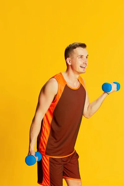 身穿橙色制服训练的年轻人的画像 呈哑铃状 背景呈黄色 健康的身体 运动的概念 健身生活方式 身体护理 — 图库照片