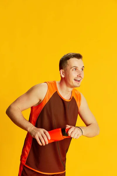 黄色の背景に隔離されたスポーツウォーターボトルでポーズオレンジの制服姿の陽気な若い男の肖像画 スポーツ フィットネスライフスタイル ボディケア アクションの概念 — ストック写真