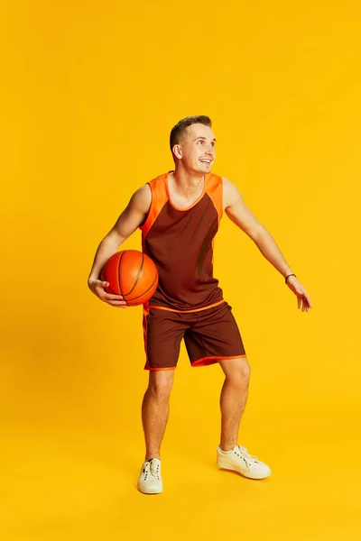 穿着橙色制服训练的年轻活跃男子的画像 在黄色背景下打篮球 团队精神运动的概念 健身生活方式 身体护理 — 图库照片