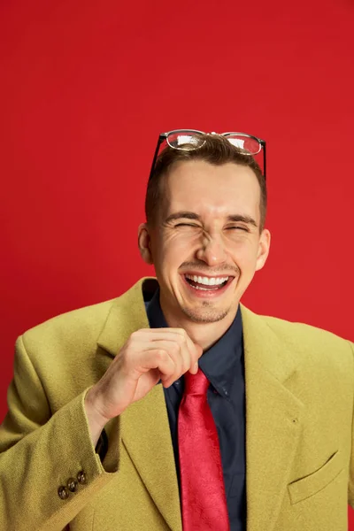 スタイリッシュなジャケットとメガネポーズで若い男の肖像画 明るく赤い背景に笑って いい冗談だ ビジネス ライフスタイル ファッションの概念 — ストック写真