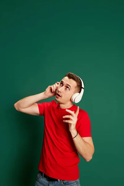 緑の背景の上に隔離されたヘッドフォンでポーズをカジュアル服の若い感情的な男の肖像画 ライフスタイル カジュアルなファッション 表情の概念 — ストック写真
